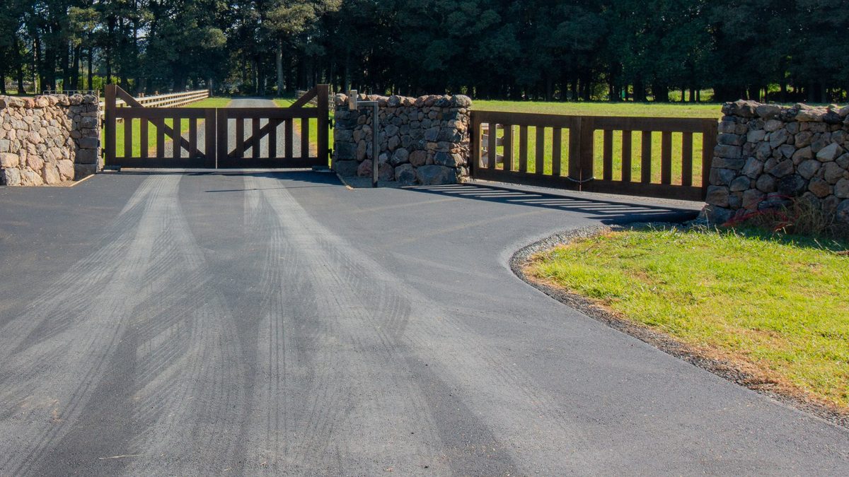 Hotmix driveway entrance with stone walls and timber gates