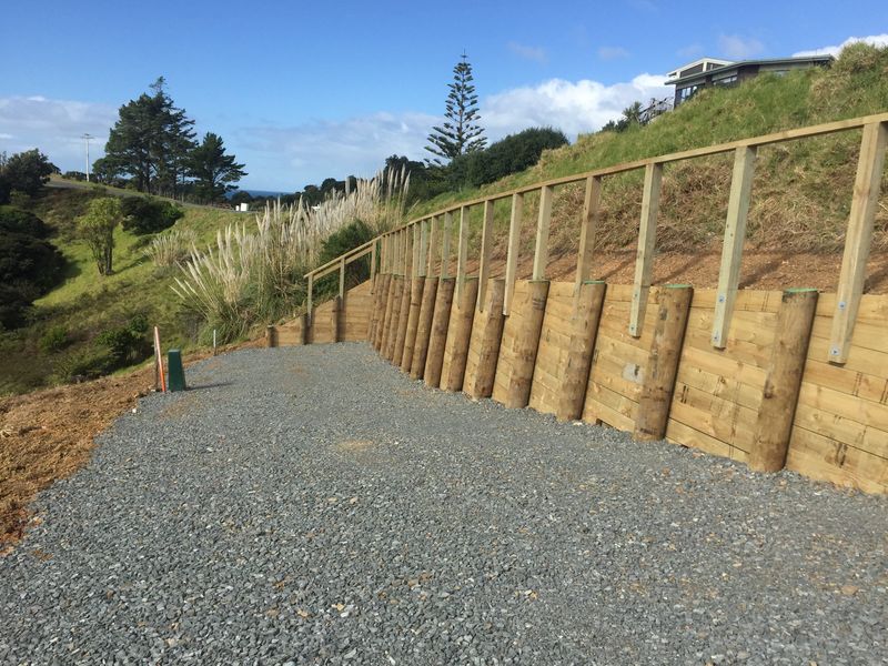 Timber pole retaining wall with handrail beside a metal path