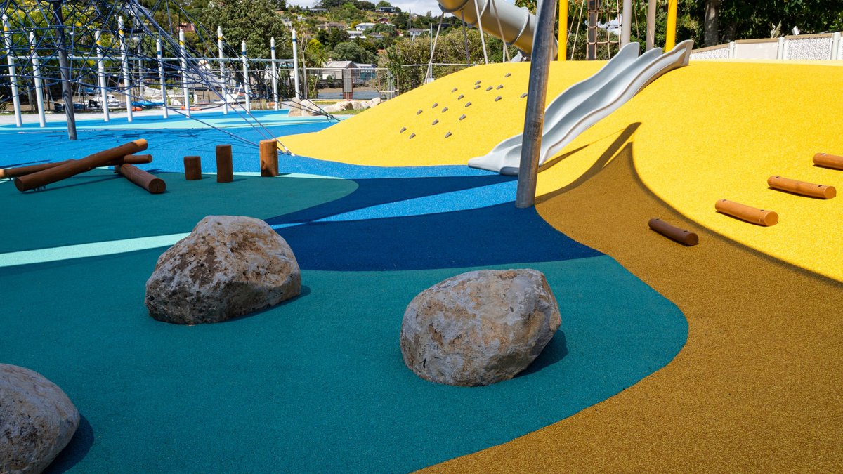 Coloured wet pour safety surfacing with rocks and a play mound