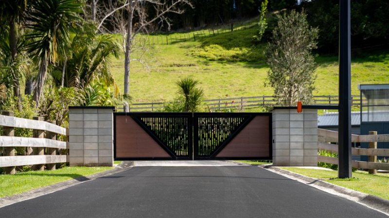 New asphalt driveway leading to a timber and steel entrance gate
