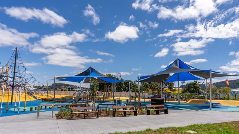 Playground with blue shade sails, a climbing net and picnic tables