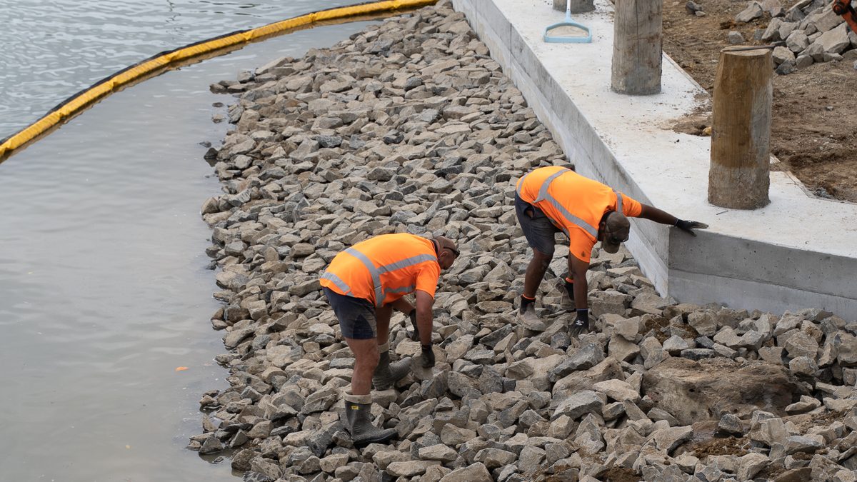Crew placing rock armour beside new boardwalk foundations on the Hātea River